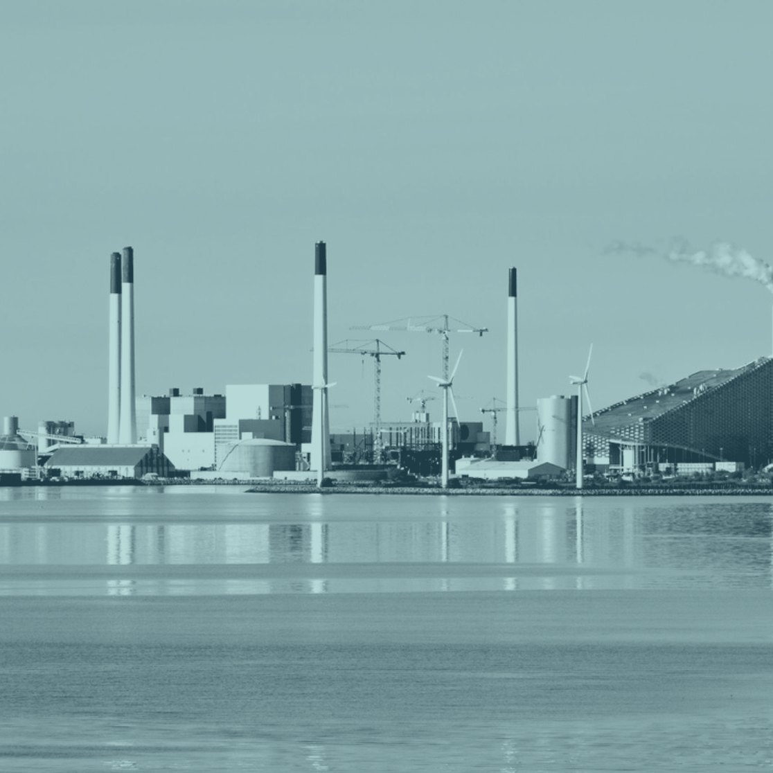 An industrial waterfront with chimneys and wind turbines
